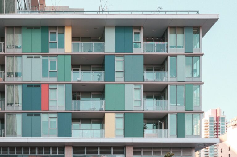 Vibrant modern apartment building facade with glass balconies under a clear blue sky.