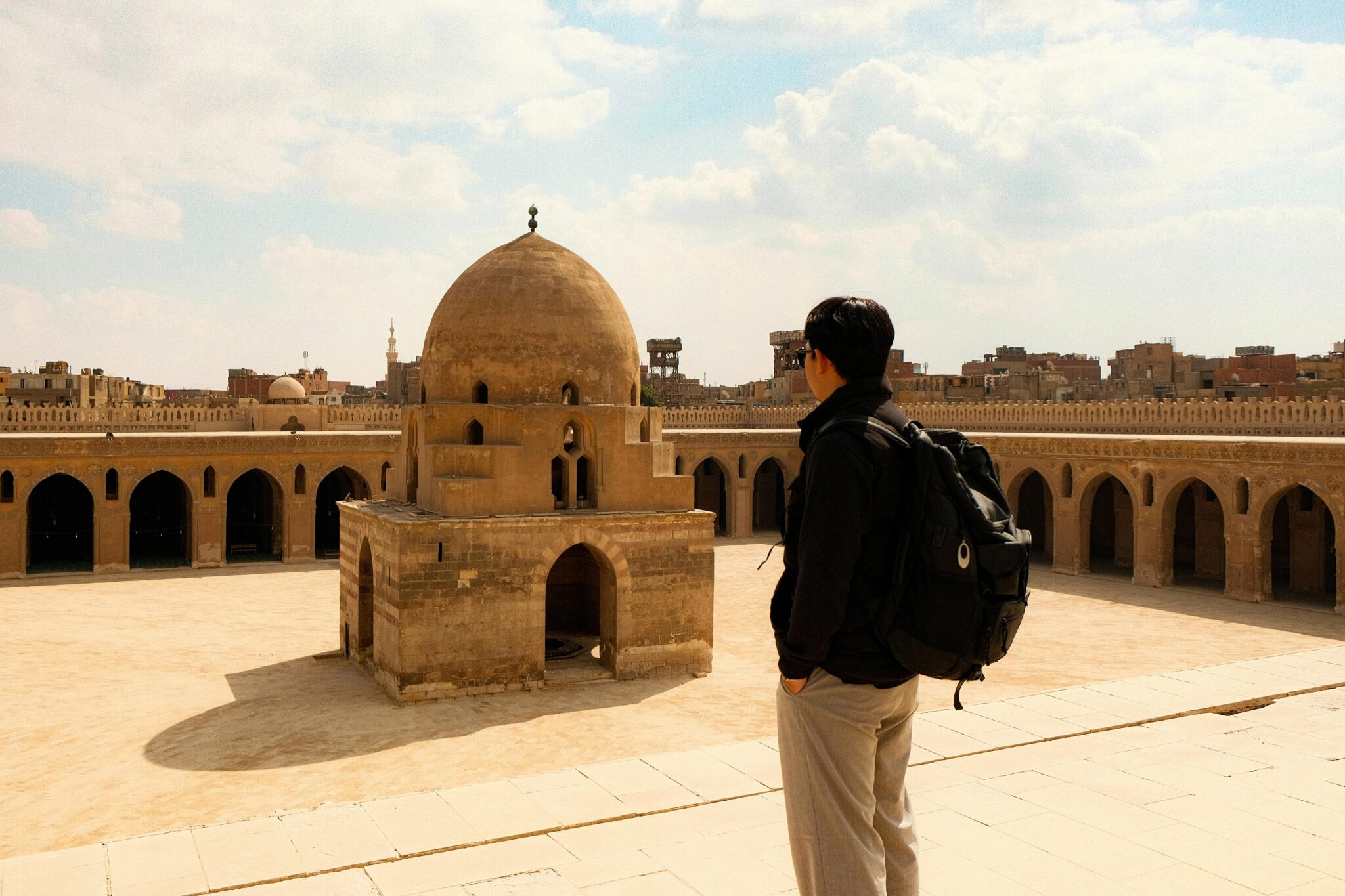 A solitary tourist admires the historic Ibn Tulun Mosque in Cairo, Egypt, under a clear sky.